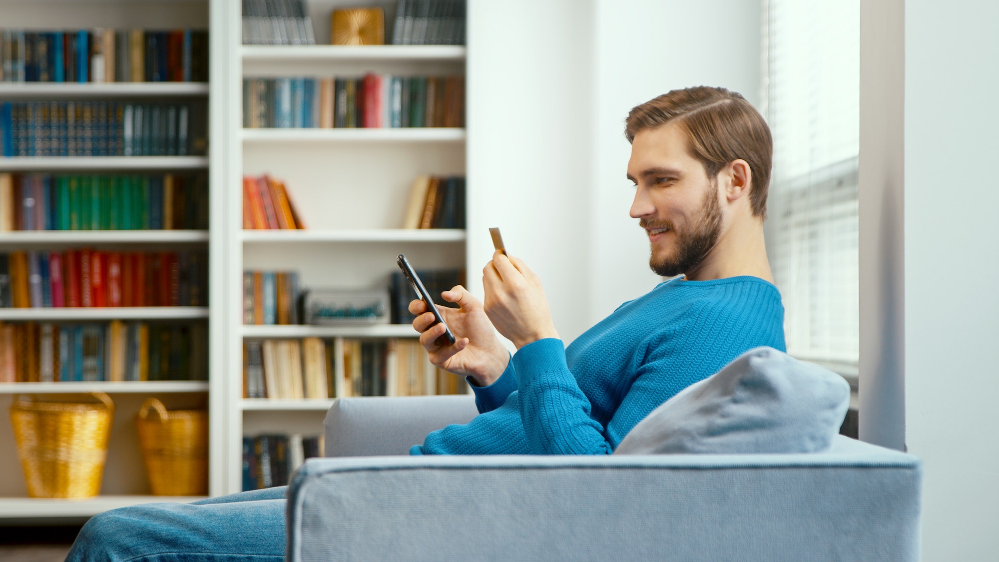 Young man looks at bank card in hand and enters digits to smartphone