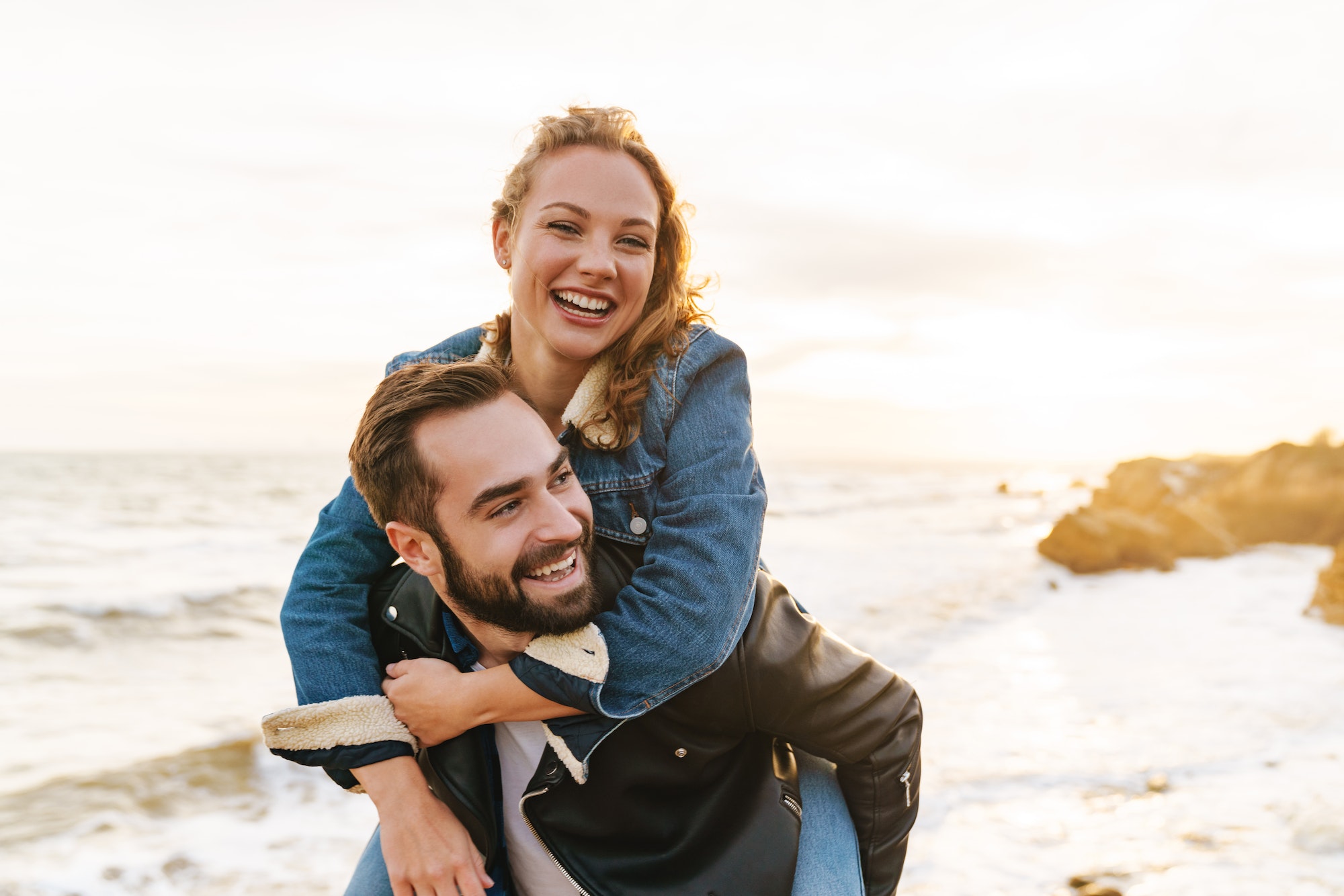 Image of beautiful young couple piggybacking while walking by seaside