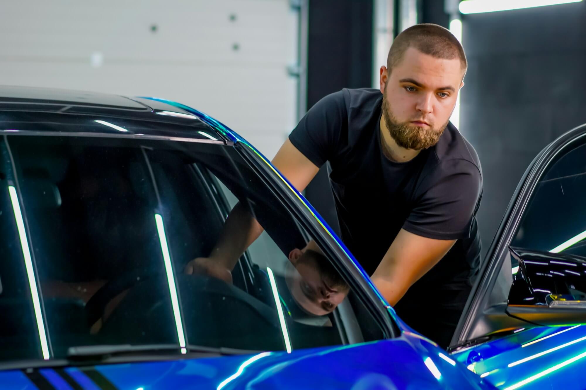An employee of a car dealership stands at the open door of a luxury car in chameleon-colored film