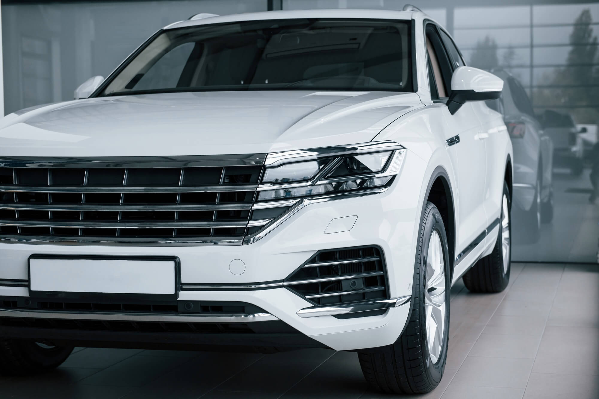 Grey glass behind. Particle view of modern luxury white car parked indoors at daytime