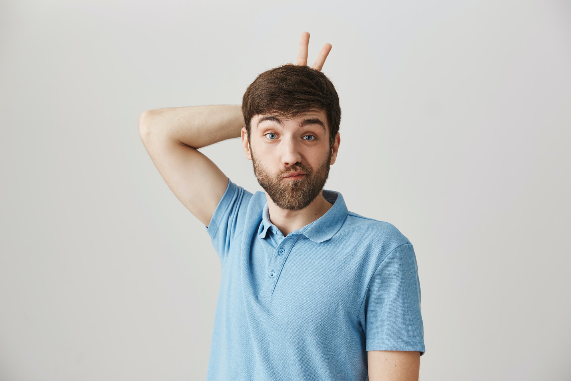 Do I look like rabbit. Funny emotive young man holding v sign behind head and making faces at camera