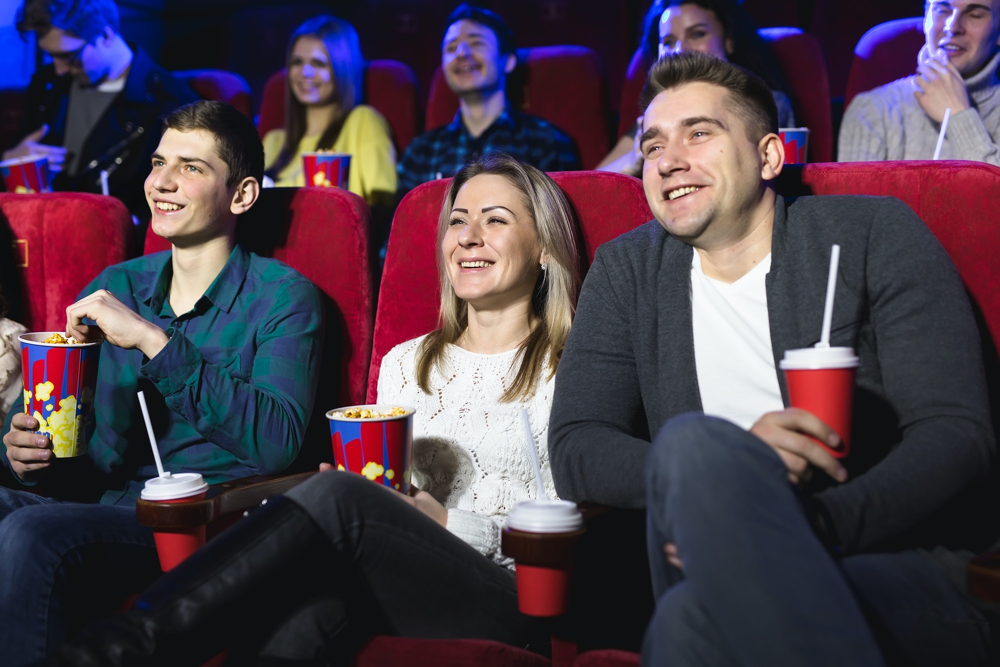Friends sit and eat popcorn together while watching movies in a movie theater