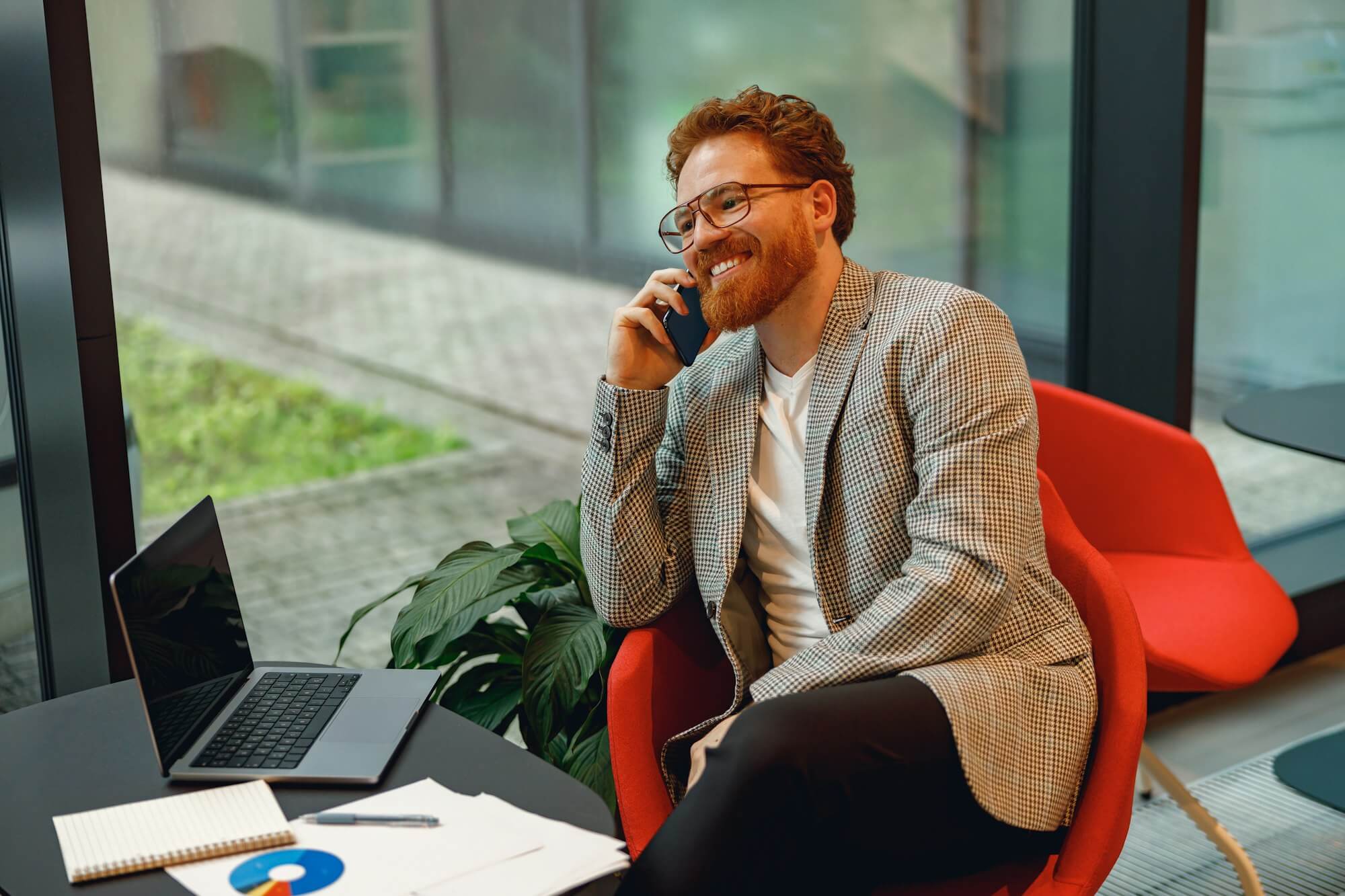 Smiling male boss talking phone with client while sitting in coworking space and working on