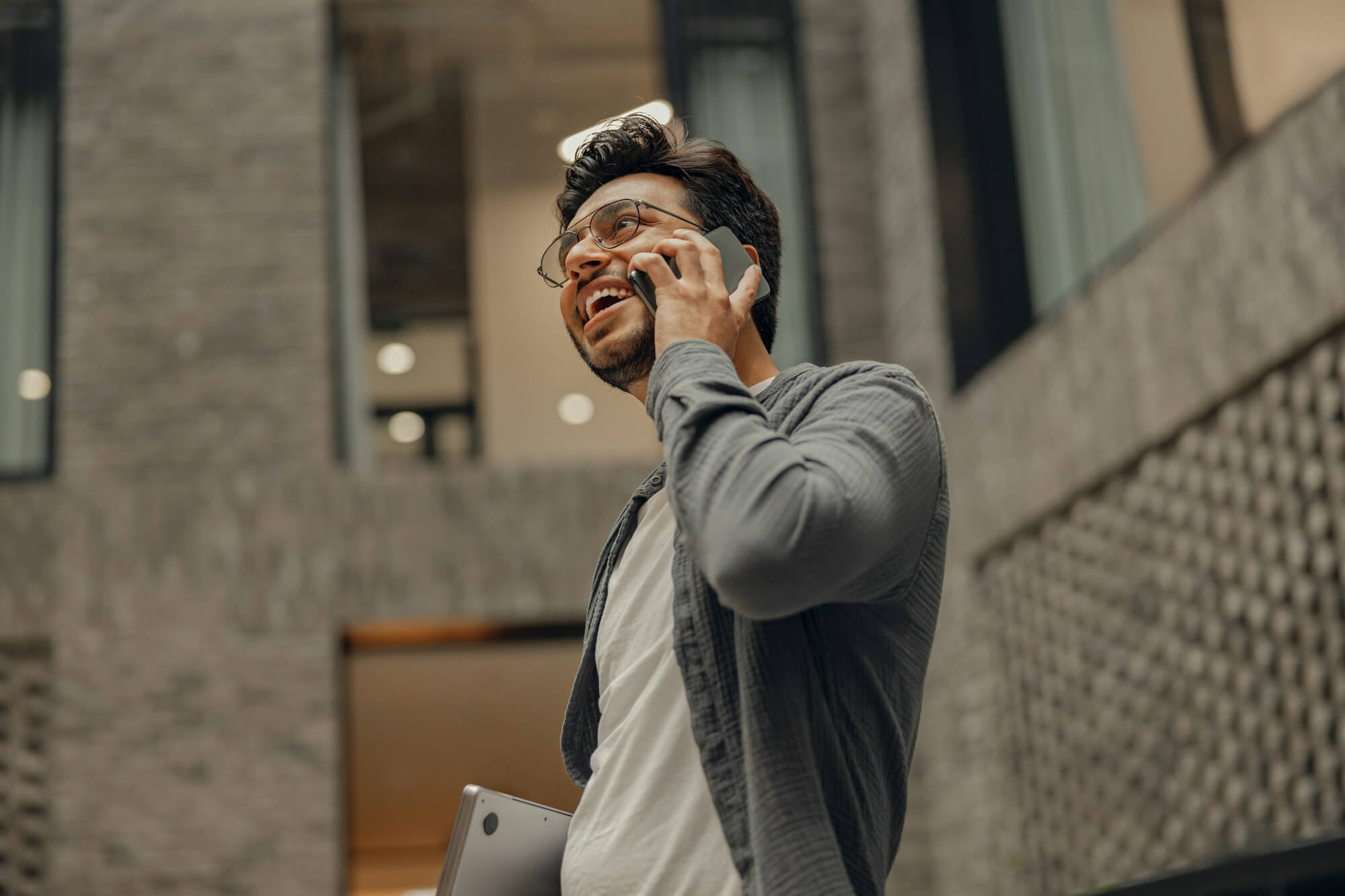 Stylish businessman in eyeglasses is talking phone standing in modern coworking space