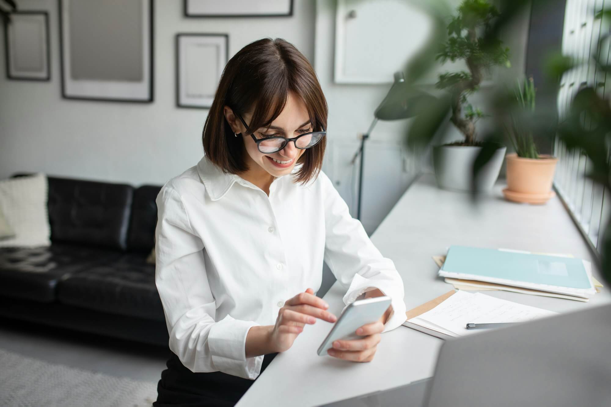 Young female employee using cellphone at workplace in office or coworking space, enjoying break at